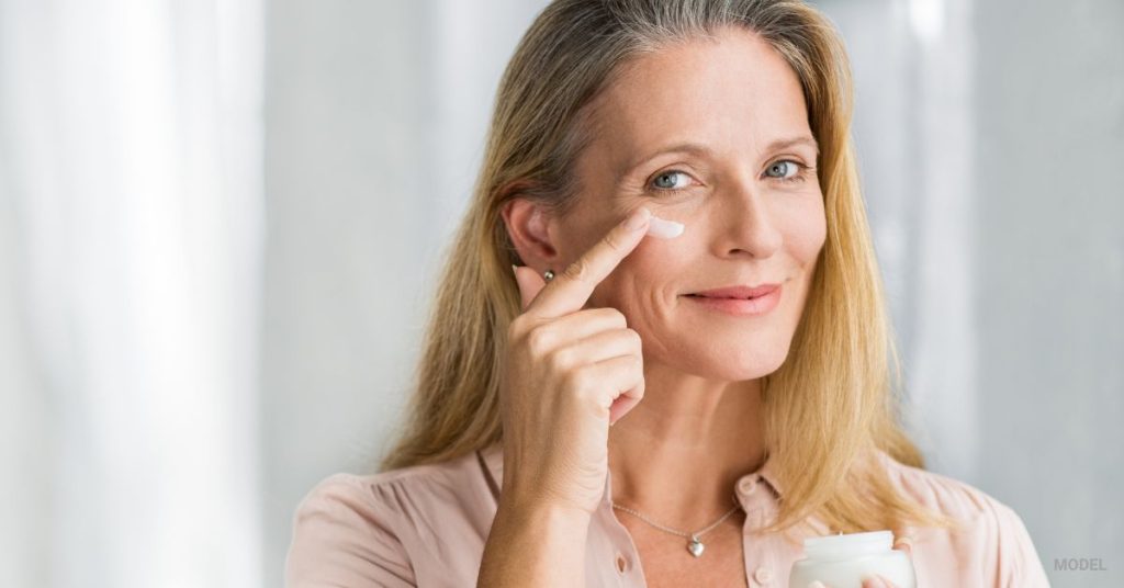 A mature woman with clear beautiful skin puts on face lotion. (Model)